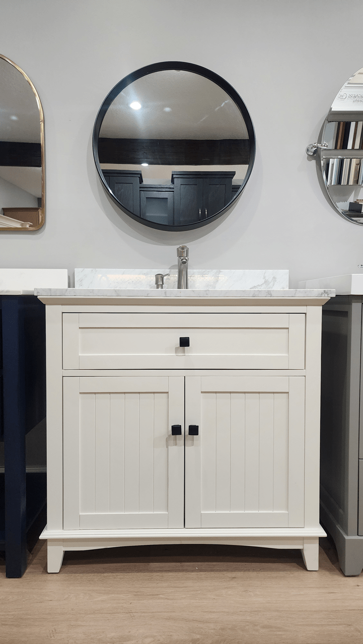 A freestanding bathroom vanity with carrara marble countertop, satin black knobs on the cabinetry, with a brushed nickel faucet and refillable soap pump.